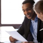 African American male and white woman discussing a sheet of paper at work.