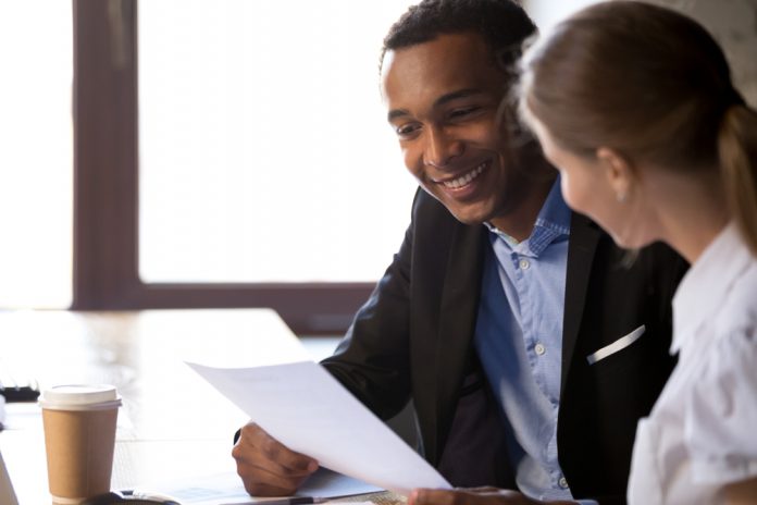 African American male and white woman discussing a sheet of paper at work.