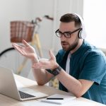 Focused,Young,Businessman,In,Eyewear,Wearing,Headphones,,Holding,Video,Call