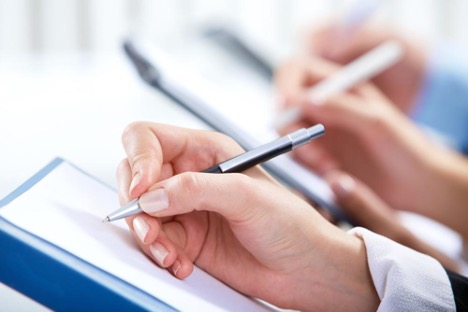 Hand holding pen about to write on a blank piece of paper with other hands in background