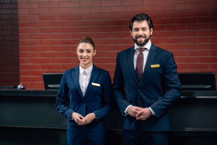 Hotel,Receptionists,Standing,Together,In,Front,Of,Counter,And,Looking