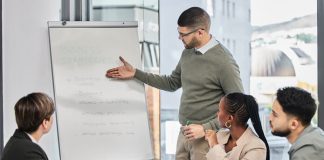 A group of board members sit at a table while a man provides training on business strategies.