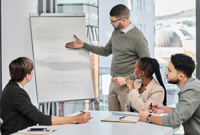 A group of board members sit at a table while a man provides training on business strategies.