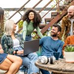 group of young diverse students sitting together in a room filled with plants.