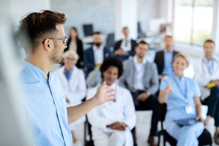 Young,Doctor,Talking,To,Group,Of,His,Colleagues,And,Business