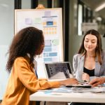 two women and a man sitting around a table brainstorming.