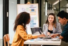 two women and a man sitting around a table brainstorming.