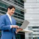 A,Smiling,Hispanic,Businessman,Stands,With,An,Open,Laptop,In