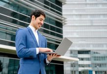 A,Smiling,Hispanic,Businessman,Stands,With,An,Open,Laptop,In