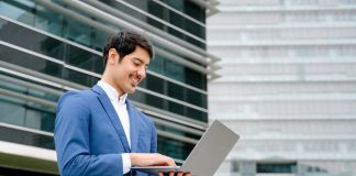 A,Smiling,Hispanic,Businessman,Stands,With,An,Open,Laptop,In