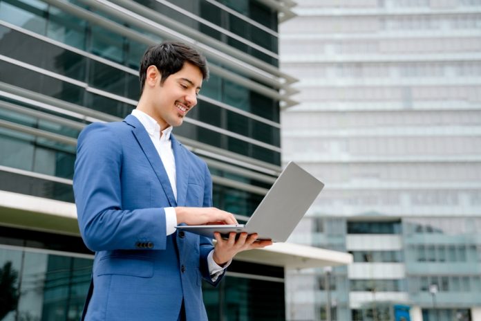 A,Smiling,Hispanic,Businessman,Stands,With,An,Open,Laptop,In