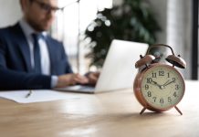 Close,Up,Of,Clock,On,Forefront,With,Businessman,Work,On