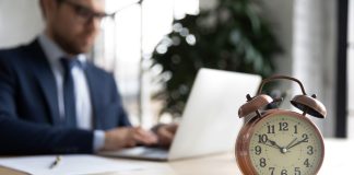 Close,Up,Of,Clock,On,Forefront,With,Businessman,Work,On