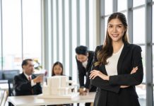 Confident,Businesswoman,With,Crossed,Arms,Smiling,In,The,Foreground,,With