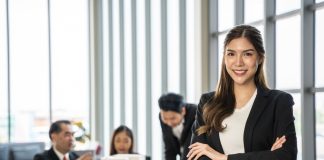 Confident,Businesswoman,With,Crossed,Arms,Smiling,In,The,Foreground,,With