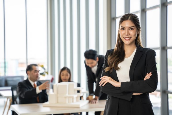 Confident,Businesswoman,With,Crossed,Arms,Smiling,In,The,Foreground,,With